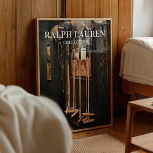 May include: A framed Ralph Lauren Collection print featuring polo mallets, equestrian equipment, and a painting of a horse. The print is displayed in a room with wooden paneling and a bed.