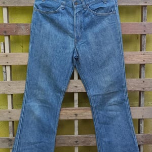 May include: Light blue denim jeans with a classic five-pocket design, hanging on a black hanger. The jeans have a straight leg cut at the top and flare out from the knee down. The jeans are made of a medium-weight denim fabric.