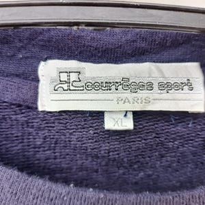 May include: Close-up of a navy blue sweatshirt with a white tag. The tag reads "courr&egrave;ges sport PARIS" with an XL size label. The sweatshirt is hanging on a black hanger.