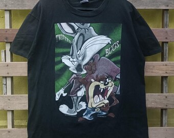 May include: Black t-shirt featuring Bugs Bunny and the Tasmanian Devil from Looney Tunes. The graphic includes the text "Twisted Bugs" in white and green. The shirt is hanging on a black hanger.