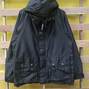 May include: Black hooded jacket with multiple front pockets and snap closures. The jacket features a zip-up front and a drawstring hood. The garment has a casual, utilitarian design, suitable for outdoor wear. The jacket is made of a durable, possibly water-resistant material.