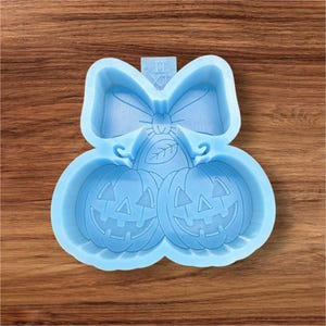 May include: A light blue silicone mold featuring two carved pumpkins with smiling faces, a bow, and a leaf design. The mold is designed for crafting Halloween-themed items.
