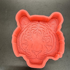 May include: Red silicone mold shaped like a tiger's face. The mold is designed for making cakes, soaps, or other crafts.
