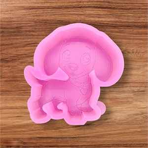 May include: A pink silicone mold in the shape of a cartoon dachshund dog. The dog has large, floppy ears, a collar with a heart pendant, and a smiling expression. The mold is designed for crafting or baking.