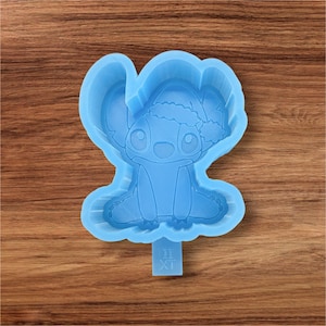 May include: A light blue silicone mold in the shape of a cartoon character wearing a Santa hat. The mold features the character's large ears, eyes, and seated pose. The base of the mold has the letters "II XT".