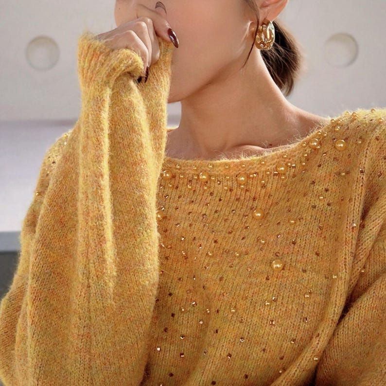 A close-up of a woman wearing a yellow sweater with gold embellishments, including rhinestones, and gold hoop earrings.