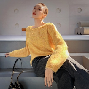 A woman wearing a yellow sweater and gray pants is sitting on a step, with a black purse next to her.