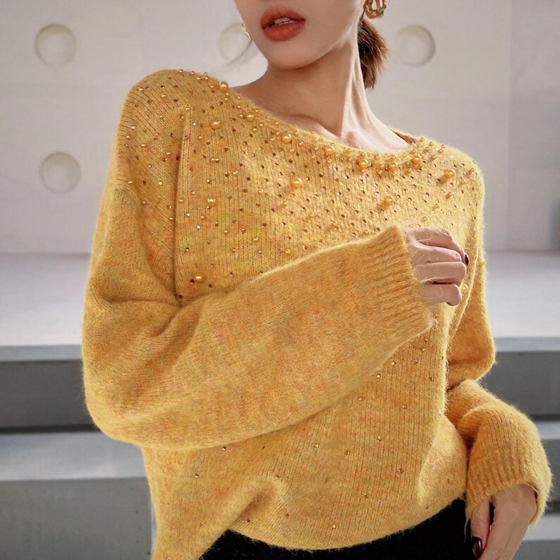 A woman wearing a yellow sweater with gold embellishments, posing in front of a white background.