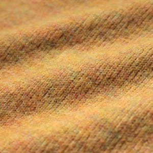 A close-up view of a textured fabric, possibly a sweater or blanket, with a warm, yellowish-orange color.