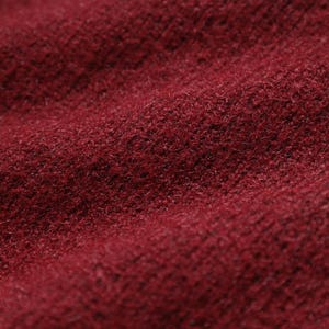 A close-up image of a red, textured fabric, possibly a sweater or blanket, with a slightly wrinkled appearance.