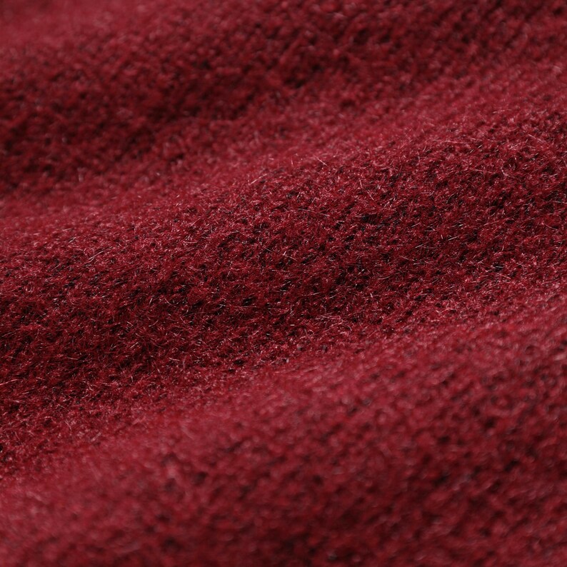 A close-up image of a red, textured fabric, possibly a sweater or blanket, with a slightly wrinkled appearance.