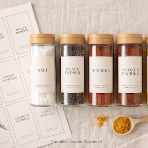 Puede incluir: Frascos de especias de vidrio con tapas de madera, etiquetados con nombres como "Sal", "Pimienta negra" y "Cúrcuma". Una cuchara de madera contiene cúrcuma, y también hay una hoja de etiquetas imprimibles y tijeras. El texto "Printable Instant Download" es visible.