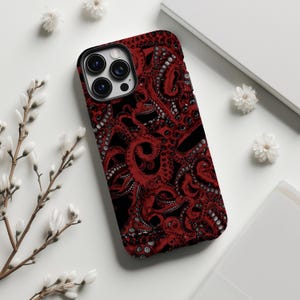 May include: A phone case with a red octopus tentacle pattern on a black backdrop. The case has a black border around the camera lenses. The design is detailed and covers the entire surface of the case.