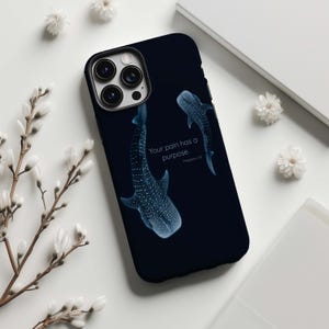 May include: A navy blue phone case featuring two whale sharks with white spots. The text "Your pain has a purpose" is printed on the case, along with the Bible verse reference, Philippians 1:29.