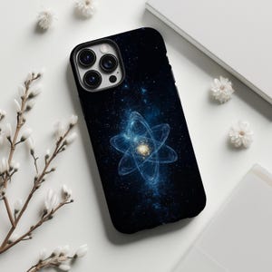 May include: A black smartphone case featuring a deep space design with a glowing blue atomic structure at the center. The background displays a dark nebula with scattered white stars, and the case has a triple-lens camera cutout at the top left.