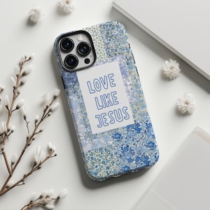 May include: A phone case with a floral pattern in shades of blue and white. The case features the text "LOVE LIKE JESUS" in blue on a white background. The case has a black camera module.