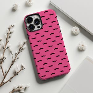 May include: A pink phone case with a repeating pattern of black mustaches. The case has a glossy finish and is designed to fit a smartphone. The case is shown on a white surface with decorative flowers.