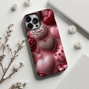 May include: A phone case featuring a pattern of various heart designs in shades of red and pink. The hearts have different textures, including dotted, textured, and smooth surfaces. The case has a camera cutout and is set against a white background.