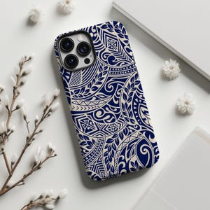 Könnte beinhalten: Eine Smartphone-Hülle mit einem marineblauen und cremefarbenen Stammesmuster. Die Hülle hat ein detailliertes Design aus geometrischen Formen, Wirbeln und blattartigen Elementen. Auf einer weißen Oberfläche mit weißen Blumen und einem weißen Notizbuch.