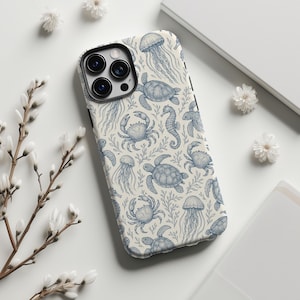 May include: A phone case featuring a repeating pattern of blue sea creatures on a cream background. The design includes jellyfish, turtles, crabs, and seahorses, with sprigs of seaweed. The case has a black border and a camera cutout.