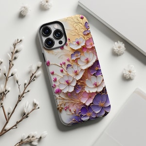 May include: A phone case with a floral design featuring white, pink, and purple flowers with gold accents. The case has a black border and a white background. The flowers are arranged in a layered pattern.