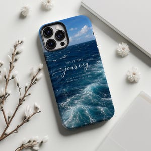 Może przedstawiać: Etui na smartfona z motywem głębokiego błękitnego oceanu z białymi grzywami fal i bezchmurnym niebem. Napis "TRUST THE journey" jest wydrukowany na biało, a pod nim mniejszy tekst "EVERY WAVE LEADS YOU WHERE YOU NEED TO BE."