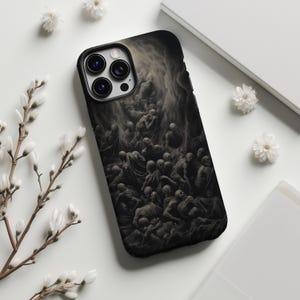 May include: Black phone case featuring a dark, detailed illustration of a crowd of figures. The case has a black border and a camera cutout. The design is a monochromatic, artistic rendering. White flowers and a white book are in the background.
