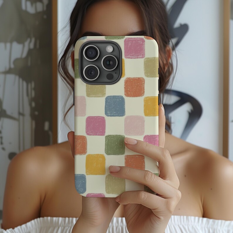 May include: A phone case with a colorful, checkered pattern. The case features a cream-colored background with squares in shades of pink, blue, green, orange, and yellow. The phone case is held up in front of a person's face.