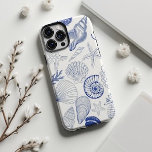 May include: White phone case with a blue seashell pattern. The design includes various seashells, starfish, and coral illustrations. The case is shown on a white surface with floral accents.