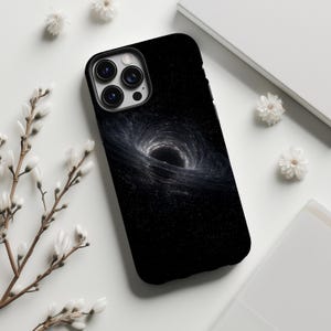 May include: Black phone case with a swirling black hole design. The case has a glossy finish and a dark background. The phone case is surrounded by white flowers and a white background.