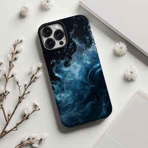 May include: Black phone case with a swirling blue and white abstract design. The case has a black border and a camera cutout. The background is white with sprigs of white flowers.
