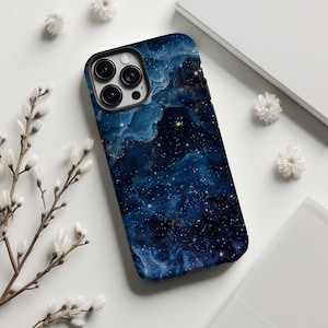 Puede incluir: Una funda para smartphone con un diseño de galaxia azul oscuro y dorado. La funda presenta un patrón de nebulosa arremolinada con estrellas dispersas, creando una estética cósmica. La funda tiene un borde negro y recortes para la cámara.