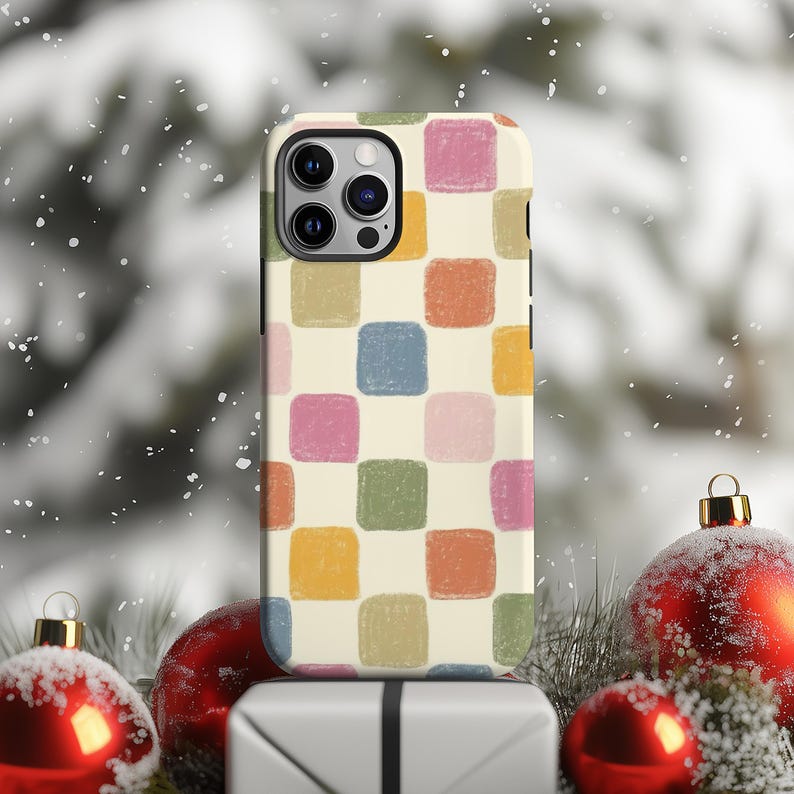 May include: A phone case with a cream-colored background and a repeating pattern of colorful squares in shades of pink, blue, green, orange, and yellow. The phone case is resting on a white gift box, with red Christmas ornaments and greenery in the background.