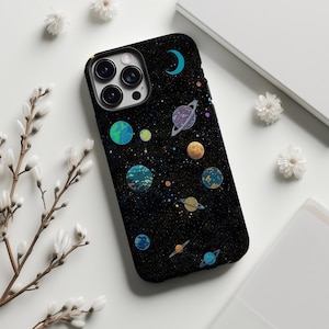 May include: A black smartphone case featuring a space-themed design with various colourful planets, a crescent moon, and scattered stars against a dark, speckled background. The case has a cutout for a triple-lens camera system on the top left.