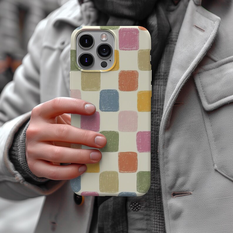 May include: A smartphone case with a cream-colored background and a repeating pattern of colorful, square blocks. The squares are in shades of pink, blue, green, orange, and yellow. The case has a camera module with three lenses.