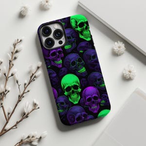 May include: A black phone case featuring a repeating pattern of neon green, purple, and dark purple skulls. The case has a glossy finish and a camera cutout. The skulls have detailed features and are set against a black background.
