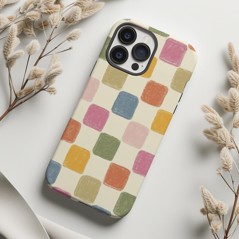 May include: A phone case with a cream-colored background and a pattern of colorful, square shapes in shades of blue, pink, orange, yellow, and green. The case has a camera cutout and a black border.