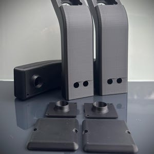 Könnte beinhalten: Eine Sammlung schwarzer, 3D-gedruckter Komponenten. Das Set umfasst zwei hohe, gebogene Teile mit quadratischen Öffnungen oben, ein rechteckiges Teil, zwei quadratische Teile mit kreisförmigen Vorsprüngen und zwei flache quadratische Teile.