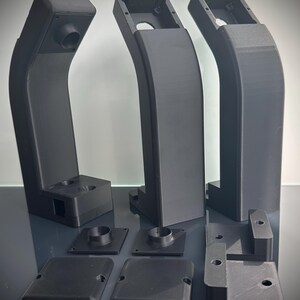 May include: A collection of black, 3D-printed components. The set includes three curved, vertical structures with rectangular tops and circular openings, along with several smaller square and rectangular pieces. The parts appear to be designed for assembly.
