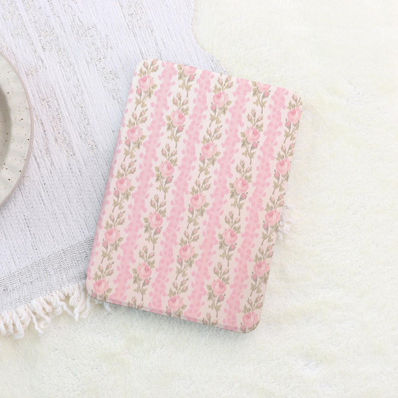 May include: A rectangular, floral-patterned case featuring a repeating design of pink roses and green leaves on a light pink and white background. The case is set on a white, textured surface.