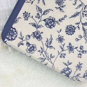 May include: Close-up of a floral patterned fabric with a navy blue border. The fabric features a cream background with a repeating pattern of navy blue flowers and leaves. The border is a solid navy blue.