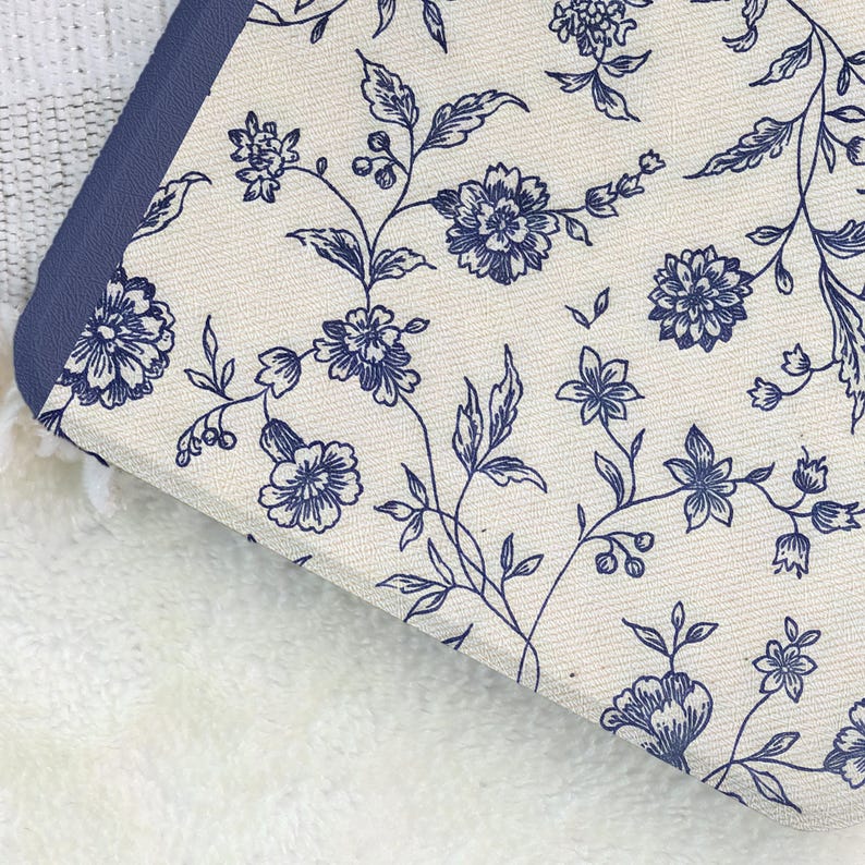 May include: Close-up of a floral patterned fabric with a navy blue border. The fabric features a cream background with a repeating pattern of navy blue flowers and leaves. The border is a solid navy blue.