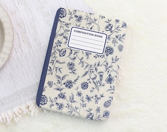 Könnte beinhalten: Ein Notizbuch mit einem blau-weißen Blumenmuster. Der Einband zeigt ein sich wiederholendes Muster aus Blumen und Ranken. Der Buchrücken ist einfarbig blau, und der Einband trägt die Aufschrift "COMPOSITION BOOK".