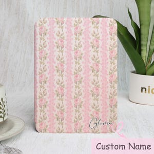 May include: A pink and cream floral patterned case with the name "Gloria" in cursive script. The case features a vertical design of pink roses and green leaves on a cream background. The words "Custom Name" are below the name.