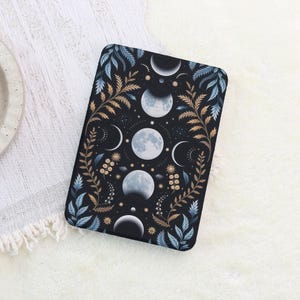 May include: A rectangular black case featuring a celestial design. The design includes phases of the moon in shades of white and gray, surrounded by gold and blue botanical elements. The case is set against a white, textured background.