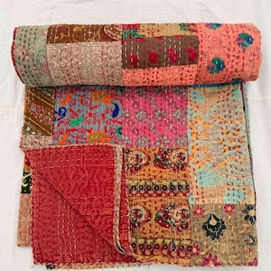 May include: A patchwork quilt featuring a variety of rectangular fabric panels in shades of red, pink, orange, yellow, and brown. The textile displays intricate floral and paisley patterns with visible white running stitch embroidery throughout.