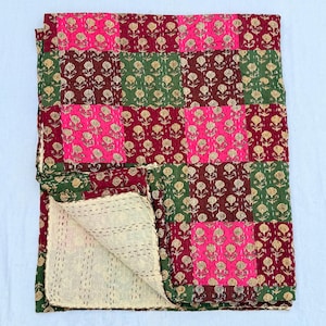 May include: A patchwork quilt featuring a repeating grid of squares in hot pink, dark red, and forest green, each printed with a small yellow floral motif. The fabric displays visible running stitch quilting patterns and a cream-coloured underside.