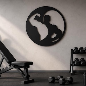 Può includere: Un allestimento per la palestra di casa con una panca pesi nera, manubri e un rack per pesi. Un'opera d'arte da parete in stile yin-yang in bianco e nero con una figura muscolosa è montata sulla parete.