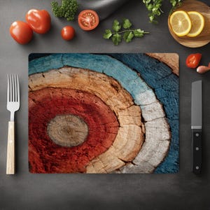 May include: A rectangular cutting board with a colorful, concentric circle design. The design features rings of red, orange, white, and blue, resembling a target. The board is surrounded by fresh tomatoes, herbs, and a knife, suggesting a culinary theme.