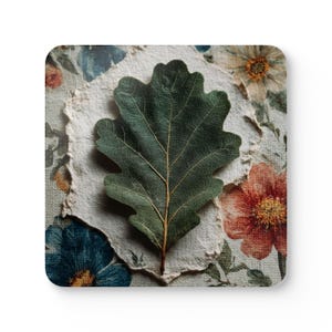 Puede incluir: Una hoja de roble verde oscuro con vetas detalladas descansa sobre un trozo de papel texturizado blanquecino. El papel se encuentra sobre un fondo floral con flores azules, naranjas y crema, creando un diseño inspirado en la naturaleza.